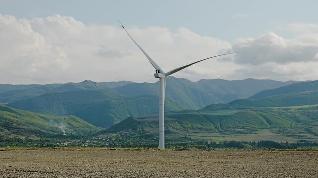 Single wind turbine rotating and producing renewable green energy against a mountain landscape with moving clouds