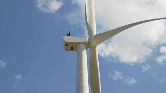 Wind turbine blades rotating producing renewable energy against a beautiful blue sky with white clouds in the background