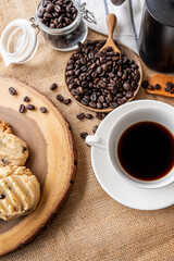 A white cup of black coffee is styled with roasted coffee beans and fresh pastries on a rustic textured tabletop. © Chaiphorn