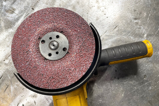 Angle grinder with abrasive disc on metal workbench background. Power tool prepared for grinding steel. Circular sanding wheel inside protective guard. Workshop equipment for metalworking jobs.