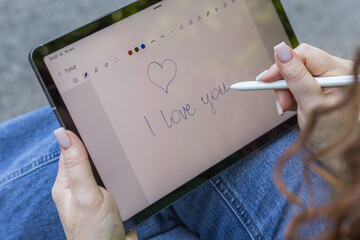 Dłoń pisząca na tablecie „I love you” z rysunkiem serca, romantyczny gest wyrażający uczucia i bliskość. © Henryk Guziak