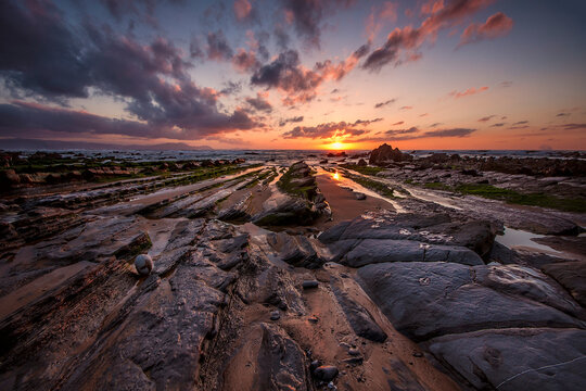 Golden sunset over the rocky flysch coastline of Barrika beach with sun reflection on wet stone platforms and ocean waves, Bizkaia, Spain