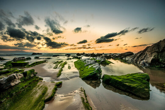 Golden sunset over the rocky flysch coastline of Barrika beach with sun reflection on wet stone platforms and ocean waves, Bizkaia, Spain