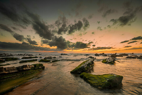 Golden sunset over the rocky flysch coastline of Barrika beach with sun reflection on wet stone platforms and ocean waves, Bizkaia, Spain
