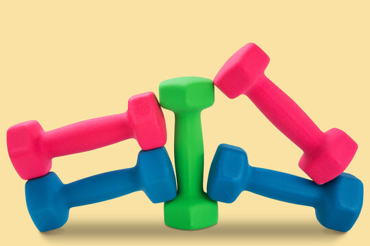 Set of colorful fitness dumbbells arranged on beige background with shadow