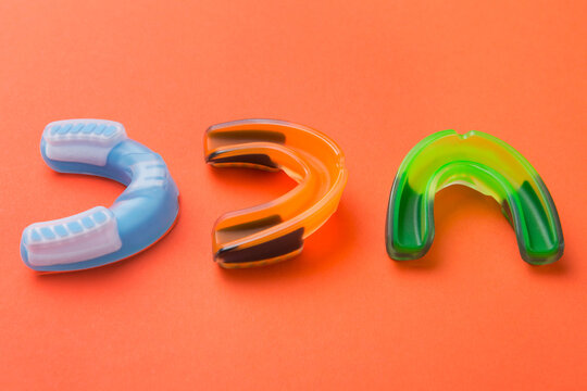 Three colorful silicone mouthguards for sports protection placed on orange background