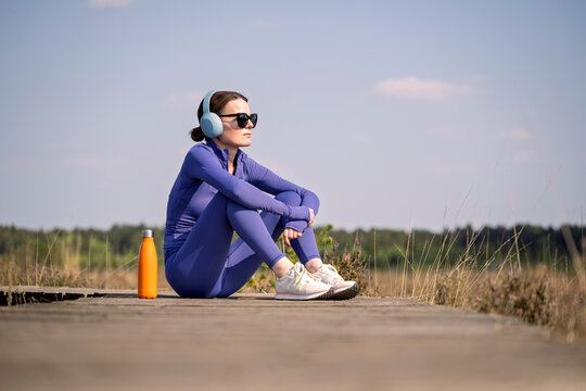Woman in Blue Sportswear Resting on a Boardwalk