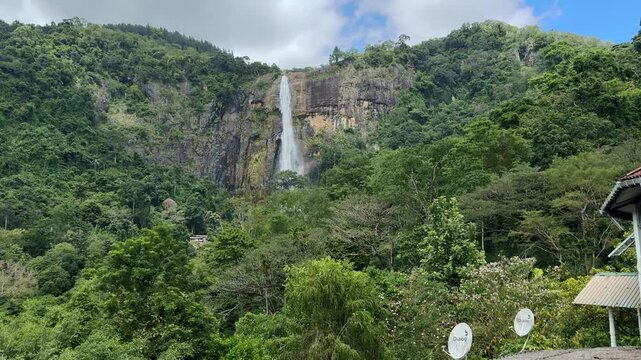Diyaluma Falls waterfall cascading down high rocky cliff surrounded by lush green tropical rainforest, Sri Lanka