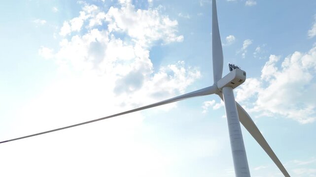 Wind turbine blades spinning with engineer performing maintenance against a bright blue sky with clouds, highlighting sustainable energy production and green jobs