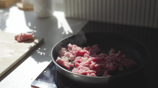 Raw meat pieces cooking in hot frying pan with steam rising. Concept of home cooking and meal preparation