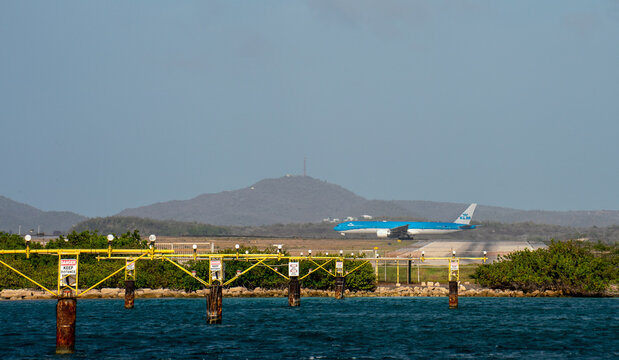 Blue and white KLM airplane taxiing on tropical airport runway