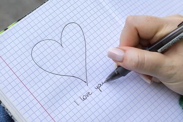 Dłoń rysująca serce na papierze w kratkę z napisem „I love you” pod spodem, romantyczny symbol miłości i uczuć. © Henryk Guziak
