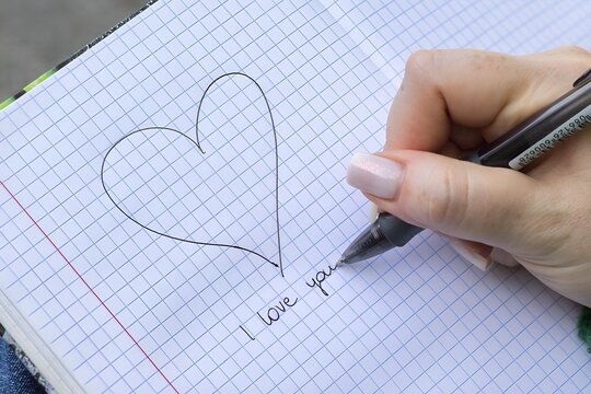 Dłoń rysująca serce na papierze w kratkę z napisem &bdquo;I love you&rdquo; pod spodem, romantyczny symbol miłości i uczuć.