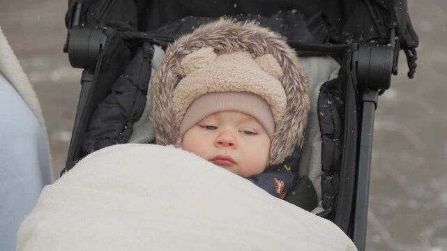 Adorable baby falling asleep in stroller during a winter snowfall