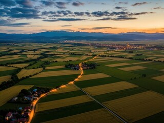 Obraz premium Aerial view of winding country road through green fields at sunset