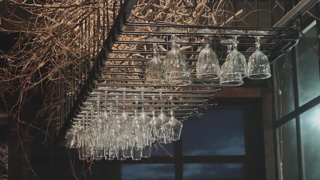 Different types of empty and clean wine glasses hanging upside down in a metal holder in a modern bar. Rustic interior with dry branches
