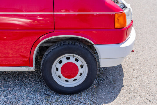 Detailed view of front portion of red and white vehicle, showcasing its wheel and lower body. Glossy red paint features decorative white stripes, with sunlight casting a shadow on the ground.