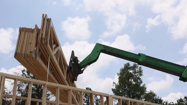 Construction crew uses crane machine to lift wooden trusses beams onto building frame