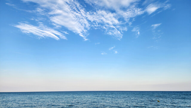 Wispy cirrus and rippled cirrocumulus clouds fill the upper sky, shaped by strong high-altitude winds. Above the clear sky and smooth sea horizon, they create a peaceful scene typical of a calm Medite