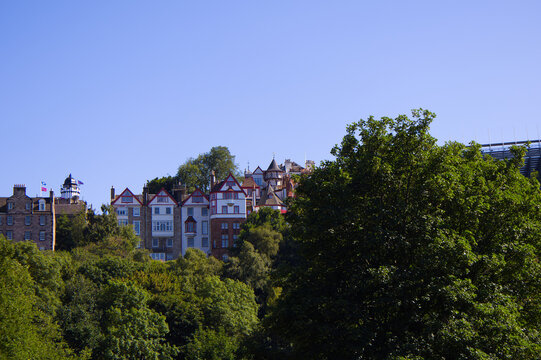 Historic Ramsay Garden white and red apartment buildings peeking above lush green trees in summer, Edinburgh Old Town architecture, UK.