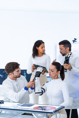 Fototapeta premium Motion capture robotics study in a minimal white laboratory: researchers examine a black robotic hand at a bench lined with scan monitors and printed reference sheets