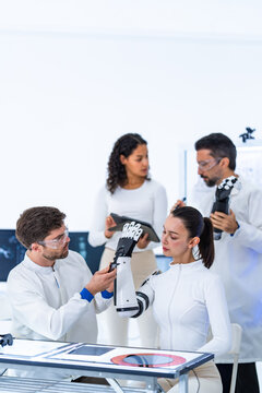 Motion capture robotics study in a minimal white laboratory: researchers examine a black robotic hand at a bench lined with scan monitors and printed reference sheets