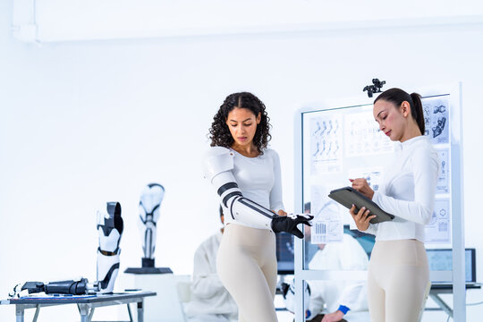 Machine perception laboratory readout, an engineer studies her tablet screen while the segmented black and white robotic forearm beside her holds its commanded pose
