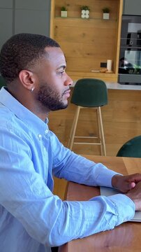 Young Black man focused at his laptop, attentively engaged in remote work from a modern home kitchen, demonstrating dedication and concentration.