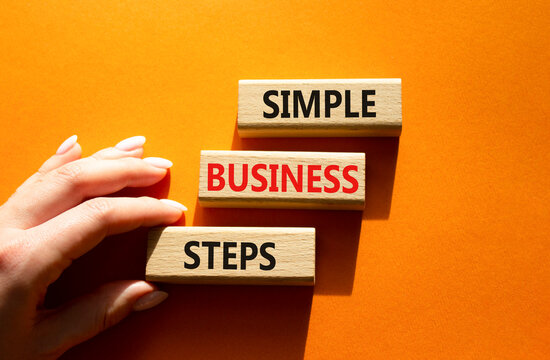 Concept words simple business steps on wooden blocks arranged as steps. Business planning concept. Businessman hand arranging wooden blocks. Orange background. Copy space.