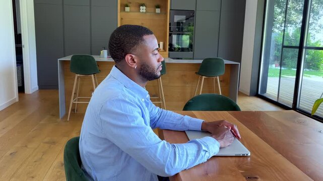 Young Black man focused at his laptop, attentively engaged in remote work from a modern home kitchen, demonstrating dedication and concentration.