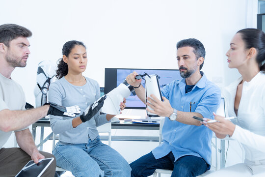 Bio-robotics laboratory: two engineers grip each other's robotic gloves to measure transferred force, a third leaning in to read the number off the wrist display