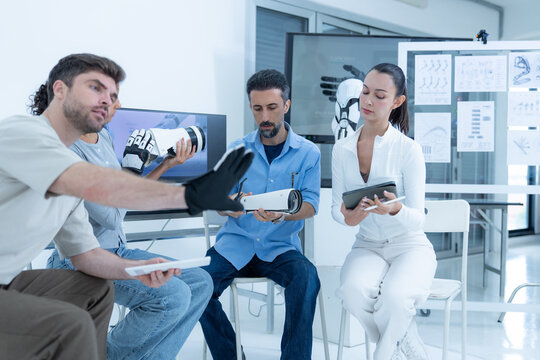 Assistive robot evaluation: a researcher holds his mechanised arm perfectly still across the aisle while the engineer sitting opposite tunes the finger tension by hand