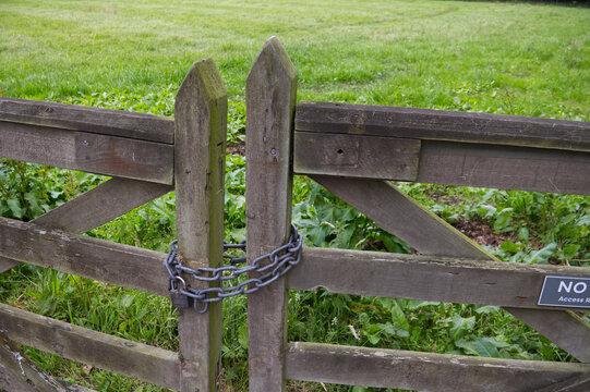 Old rustic wooden farm gate locked with a heavy metal chain and padlock. Security, restricted area and private property concept.