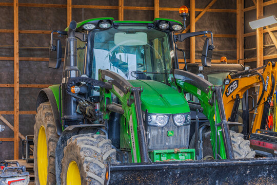Close-up view of John Deere tractor with front loader parked beside JCB excavator inside barn. Sweden. Stockholm. 