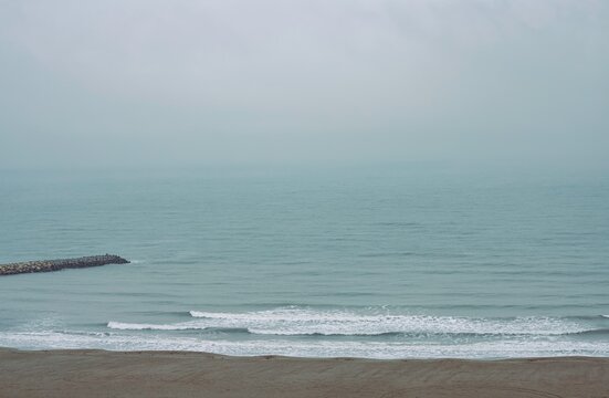 Fog covers the sea along the coast of Constanta, Romania, with distant waves meeting the grey sky, creating a subdued atmosphere that evokes reflection and introspection