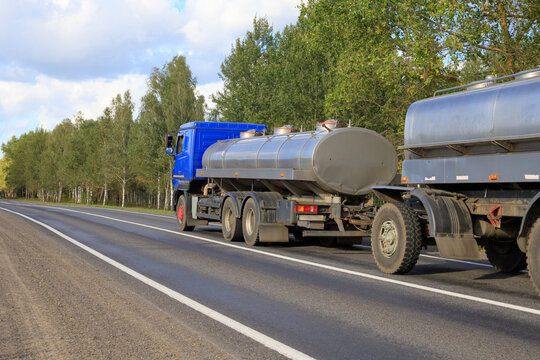 Milk tanker with a trailer travels along a highway through a wooded area in summer
