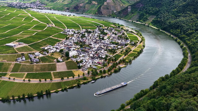 Luftaufnahme der Moselschleife bei Minheim mit einem langen Binnenschiff auf dem Fluss, umgeben von gr&uuml;nen Weinbergen und einem Weindorf im Sommer.