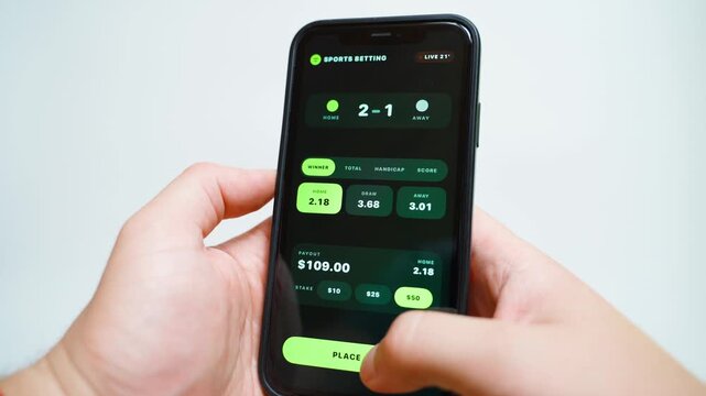 Sports betting app on smartphone with live odds and stake selection close-up. Hands holding phone with match score and payout
