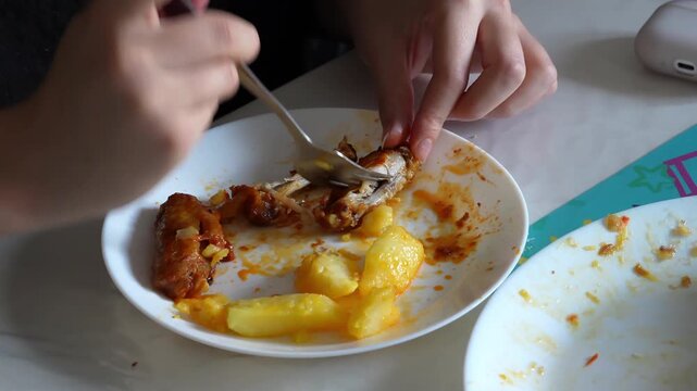 Young woman eating fried chicken wings with a fork from a plate. Boiled potatoes and crispy chicken wings served together as a hearty homemade meal. Close-up food scene, everyday dining and comfort fo