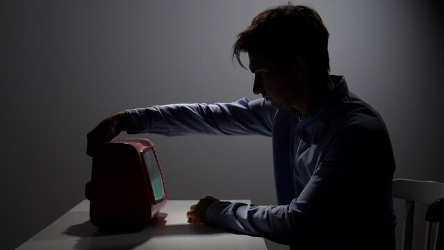 Man reaching for a retro television, casting a strong silhouette in a dimly lit room, symbolizing concepts of nostalgia, isolation, and communication disconnect