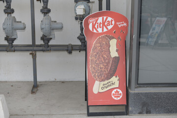 Obraz premium gas pipes and sidewalk a-frame poster sign of Kit Kat Double Crunch outside Friends Corner Convenience Store, 34 Freeland St (The Prestige), Toronto