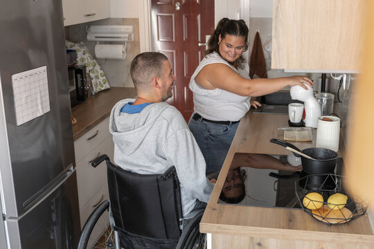 Two people are in a kitchen preparing a meal. Personal assistant helps person with disability using wheelchair.