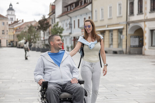 Female personal assistant helps a man in a wheelchair move through a city street. They enjoy being out and about.