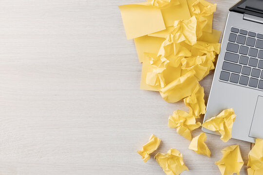 Laptop and crumpled sticky notes on a pale desk with copy space