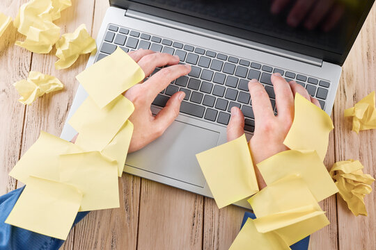 Hands type on a laptop covered with sticky notes in a home office