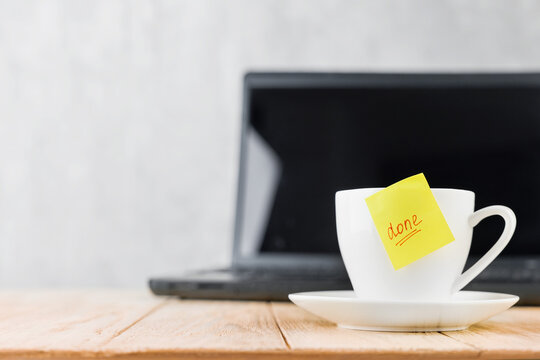 Done sticky note on a coffee cup in front of a laptop after finishing work