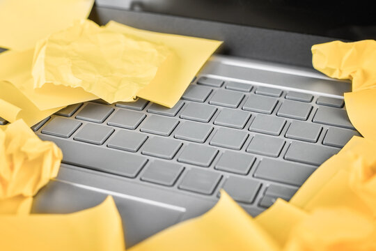 Crumpled sticky notes cover a laptop keyboard in a work overload close-up