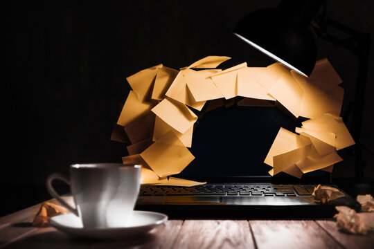 Sticky notes overflow a laptop under a lamp in a late burnout scene