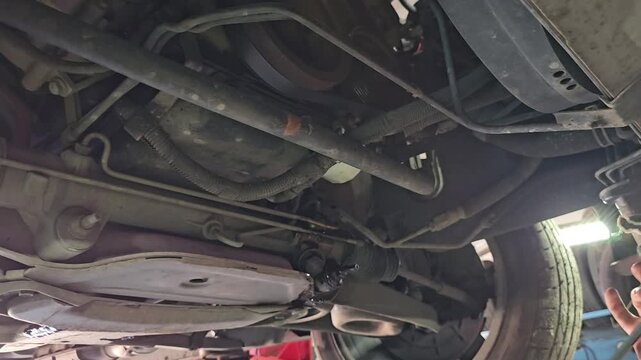 Car maintenance work under the vehicle in a workshop setting with tools and equipment visible