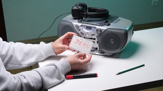 Hands holding a cassette labeled demo next to a retro boombox and headphones, ready to record or play musicnostalgic analog audio setup for home studio or mixtape creation